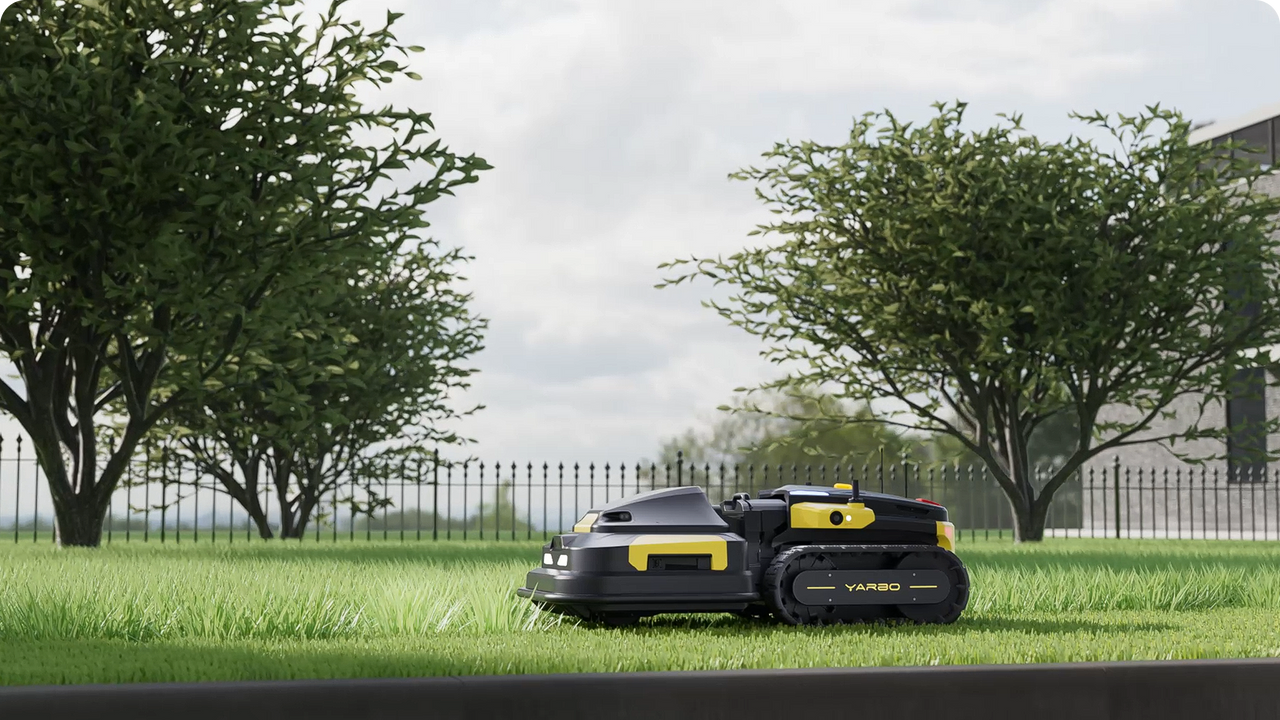 Sleek black and yellow Yarbo robotic mower glides across lush green lawn, framed by trees and a black iron fence.
