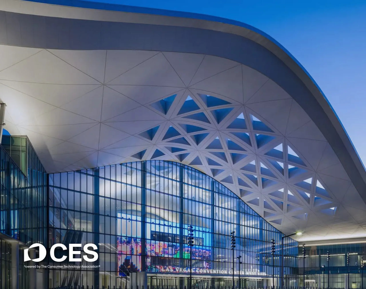 Modern white arched roof with geometric patterns over glass facade of Las Vegas Convention Center West Hall at dusk, CES logo visible.