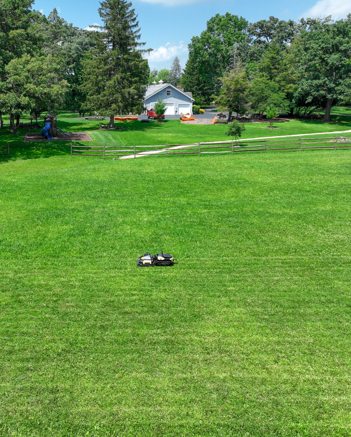 Black and yellow robotic lawn mower by Yarbo on lush green grass in a spacious backyard, side view, outdoor lifestyle scene