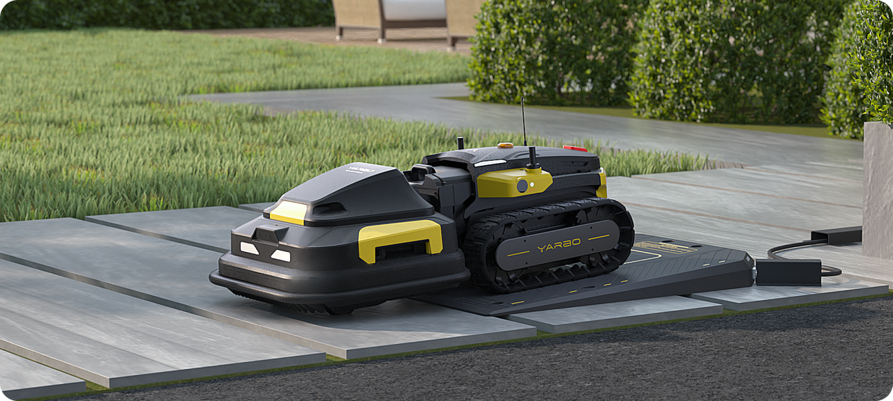 Black and yellow YARBO robotic lawn mower on charging dock in garden, surrounded by green grass and shrubs.
