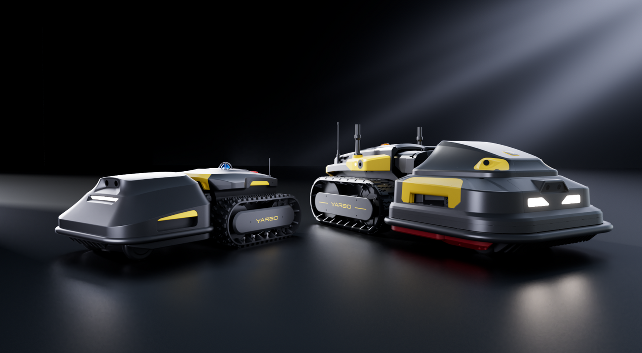 Two gray and yellow YARBO robotic vehicles with tracks, illuminated headlights, and antennas, on a dark reflective surface under spotlight.