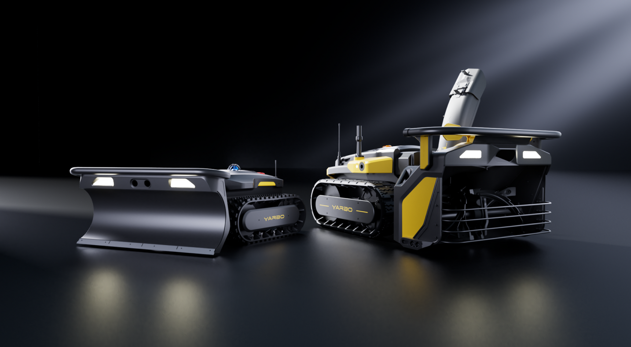 Two YARBO robotic vehicles with tracks, one featuring a plow and the other a robotic arm, displayed on a dark reflective surface under spotlight lighting.
