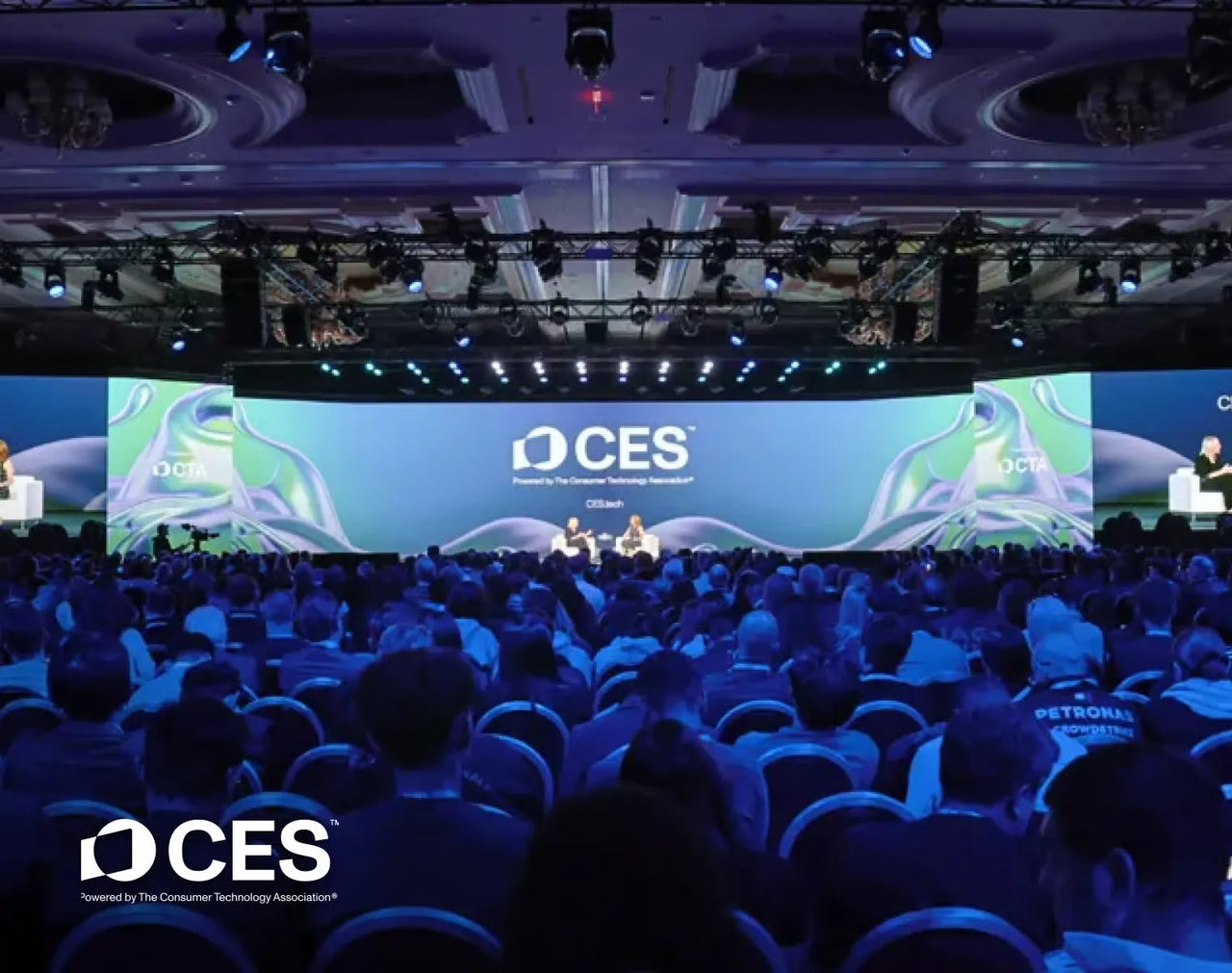 Large audience at CES conference, seated facing stage with CES logo and speakers under blue lighting.