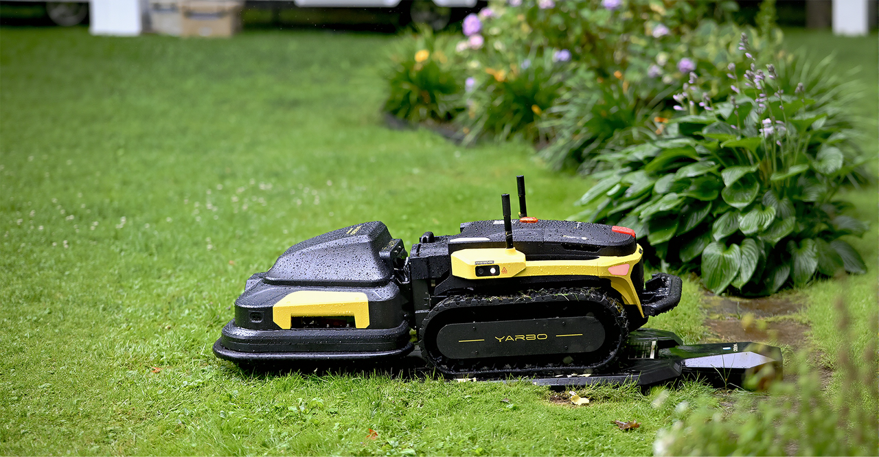 Black and yellow robotic lawn mower on wet grass near garden flowers, highlighting maintenance challenges.