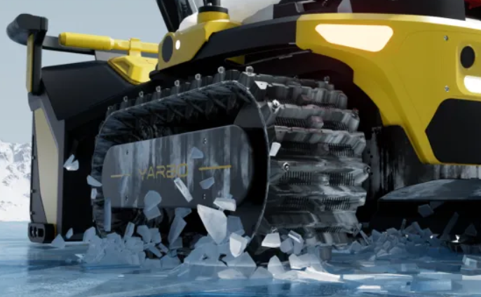 Yellow and black tracked snow blower powers through deep snow, crushing ice with rugged treads in a wintry landscape.