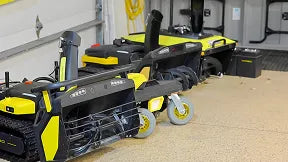 Yellow and black Ryobi power tools on wheels in a garage, with cordless drills and storage cases nearby.