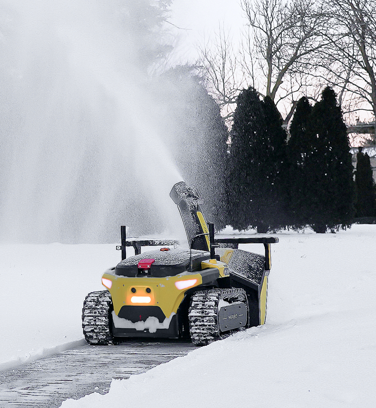 Yellow and black snow-clearing robot with glowing headlights ejects snow from its chute onto a snowy driveway, surrounded by evergreen trees.