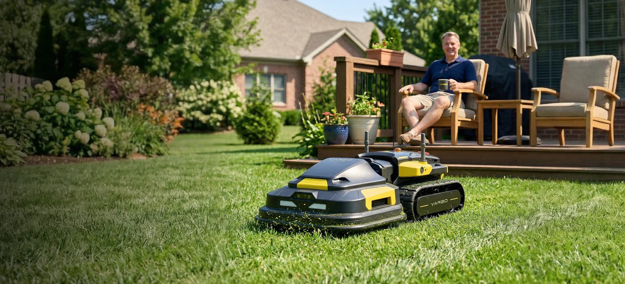 Black and yellow YARBO robotic lawn mower on green grass, man relaxing on deck in background.