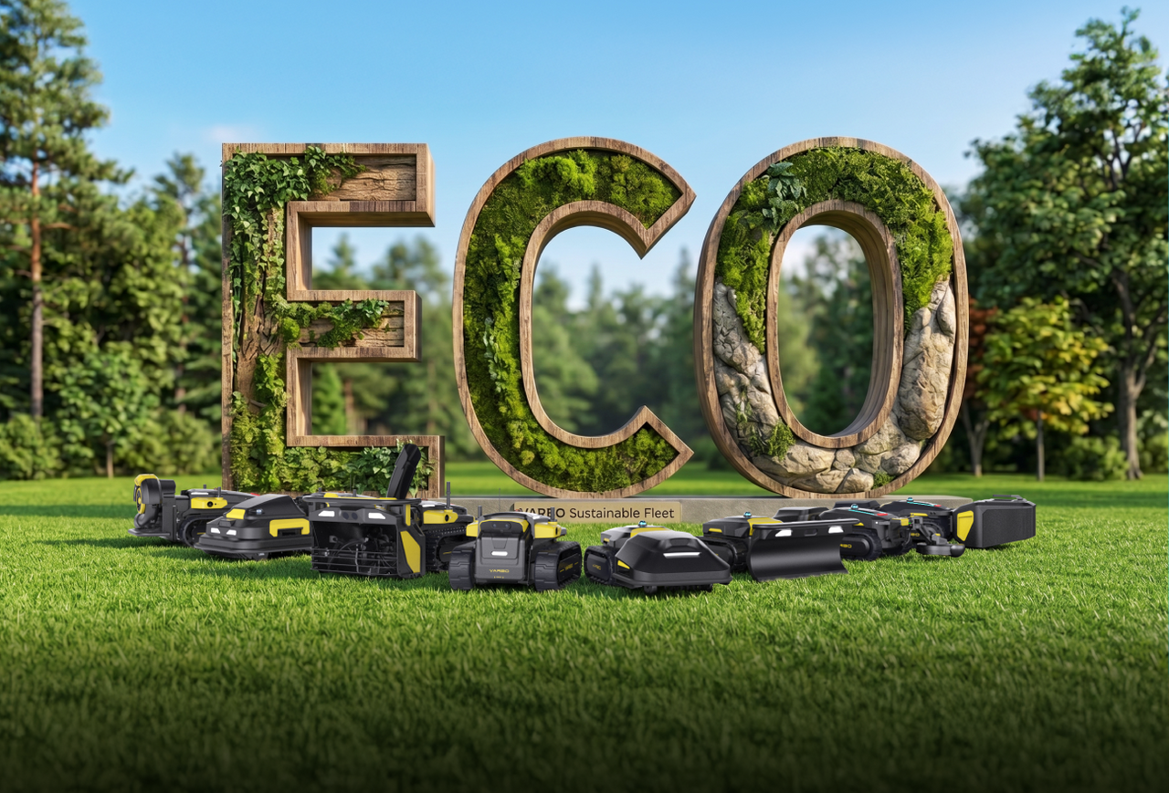 Large wooden "ECO" letters covered in green moss and ivy, with black and yellow robotic lawn mowers lined up in front on grass, under a clear blue sky.