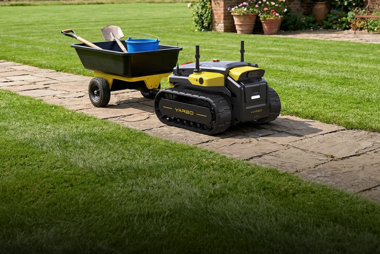 Black and yellow YARBO robotic lawn mower on stone path beside green lawn, near wheelbarrow with shovel and blue bucket.