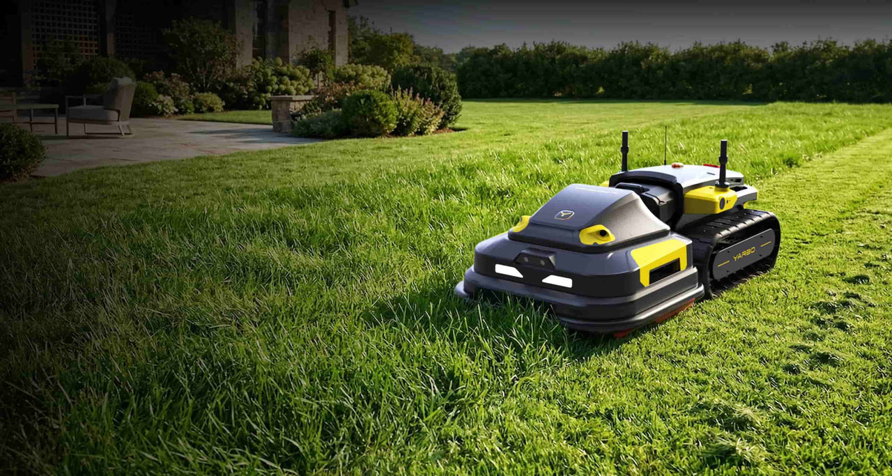 Black and yellow YARBO robotic lawn mower on lush green grass near a patio and garden.