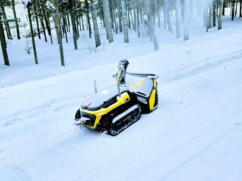 Yellow and black YARD robot on snowy path in winter forest, tracks visible, trees in background.